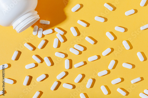 White pills are poured from a jar on a yellow background. Food supplement, multivitamins, medications