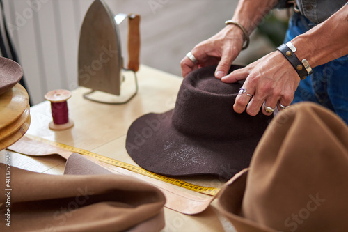 hat sewing by designer in workshop, cropped male making handmade hats, professional atelier giving shape to hat