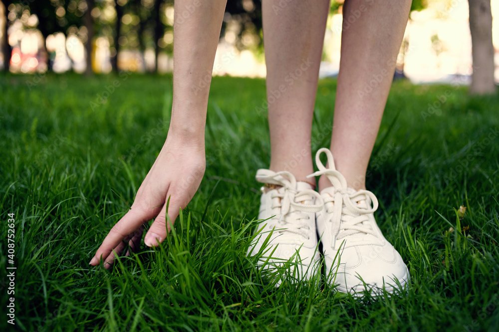 Woman in white sneakers in the park walk green grass