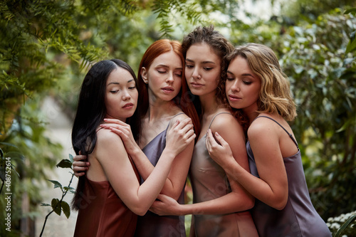 four sensual ladies in elegant silk dresses in the forest, beautiful women with healthy radiant skin, long natural hair. models posing in flowering garden