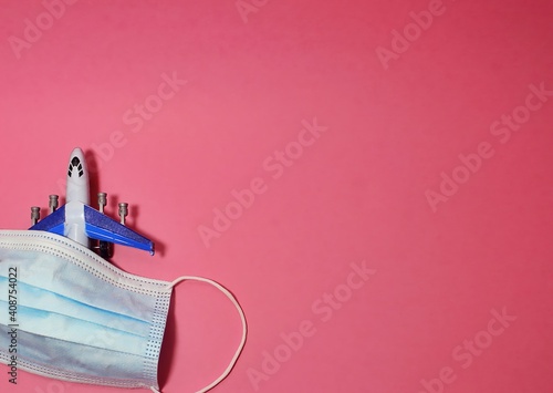 Top view of toy airplane and medical mask on light pink background with space for text. Travelling during coronavirus pandemic. Copy space. Selective focus