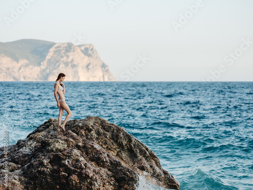 woman stands on a high rock in nature near the sea and a mountain in the backgroun © SHOTPRIME STUDIO