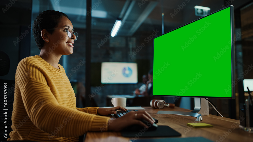 Young Multiethnic Specialist Working on Desktop Computer with Green Screen Mock Up Display in Creative Office. Beautiful Diverse Female Manager with Short Hair and Glasses is Wearing a Yellow Jumper. Young Multiethnic Specialist Working on Desktop Computer with Green Screen Mock Up Display in Creative Office. Beautiful Diverse Female Manager with Short Hair and Glasses is Wearing a Yellow Jumper.