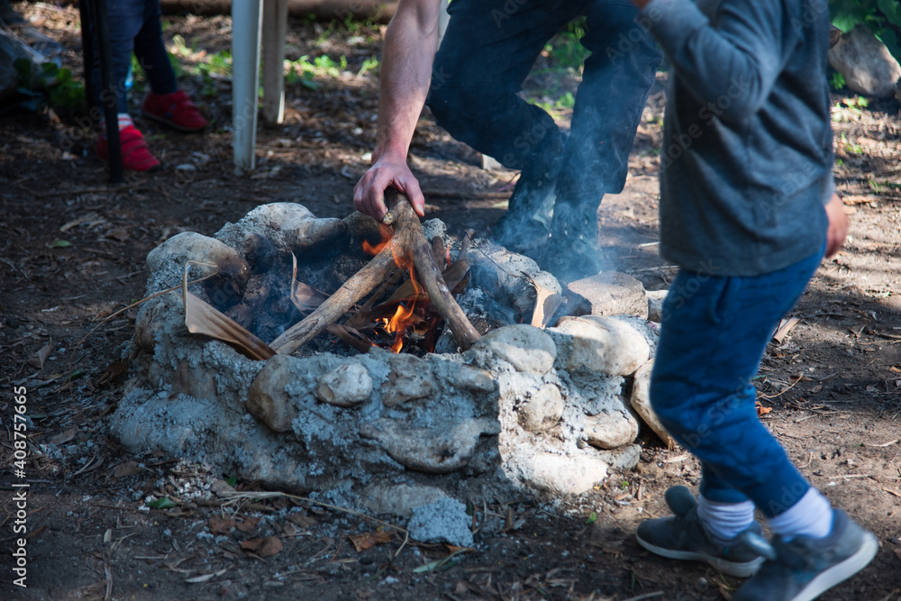 Obraz premium Cooking baked potatoes on fire in hot coals. Buried tasty vegetables in foil in bonfire on picnic. Vegetarian food outdoors. Wrapped fried potatoes on fire, barbecue. Food in forest, evening dinner