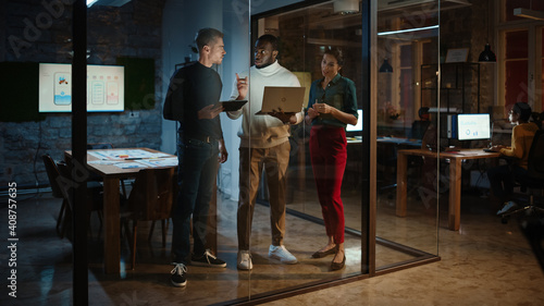 Diverse Multiethnic Team are Having a Conversation in a Meeting Room Behind Glass Walls in an Office. Black Creative Director Talks to Project Managers About the Work and Shows Brief on Laptop.