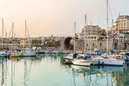 View to Heraklion in the early morning during sun rise, the old port with traditional fishing boats and town with its antient buildings at the background.