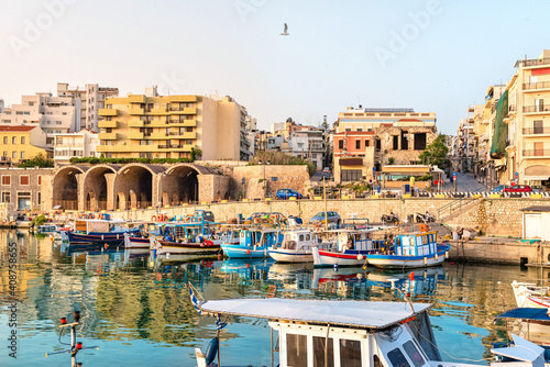 View to Heraklion in the early morning during sun rise, the old port with traditional fishing boats and town with its antient buildings at the background. 
