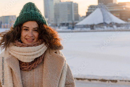 Young woman with dark curly hair in a winter hat, warmly dressed, winter frost, sunny day outside. photo