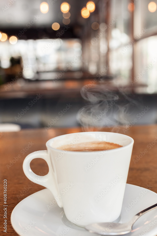 Coffee in a cafe on a wooden table. Drink with steam, smoke. Beautiful blurry background with sideways. Sunlight, interior. Delicious Hot Americano