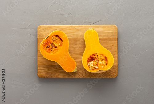 Raw organic butternut pumpkin or gramma cut in half close-up on wooden board on gray concrete background, top view, copy spase