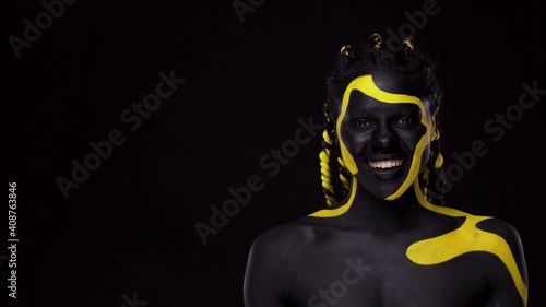 Face art. Woman with black and yellow body paint. Young african girl with colorful bodypaint. An amazing afro american model with yellow makeup. photo