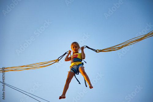 A little cheerful girl flies on springy bright elastic bands and jumps on a trampoline enjoying the long-awaited vacation in the warm sun