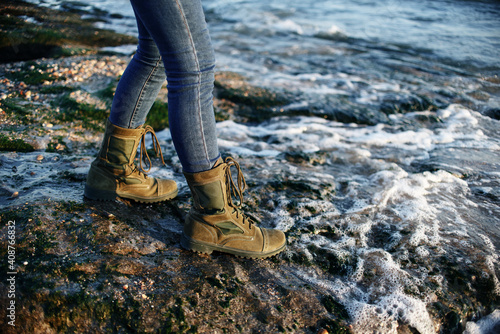 Man in jeans and green boots on laces in a military style walks on the seashore