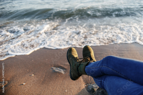 People in green boots on military-style shoelaces and jeans sits on the seashore
