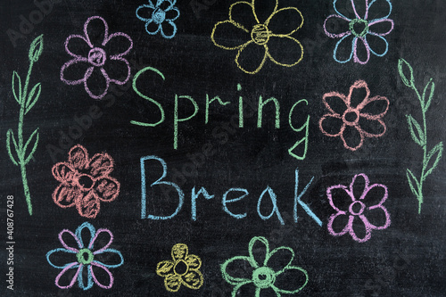 Spring break with flowers written in colorful chalk on a black chalkboard. Spring Break Concept
