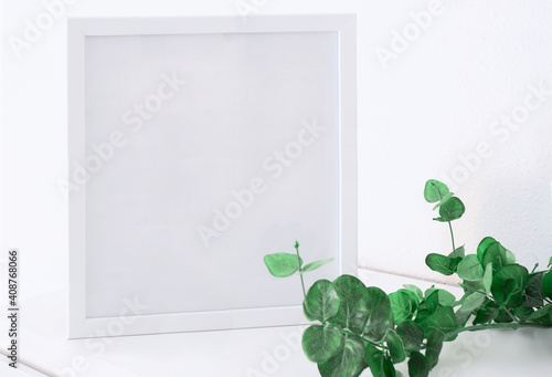 White square frame mockup with a eucalyptus plant i on a white table.Copy space