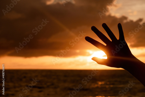 Silhouette of a hand raised to the sky The sea and the evening sun, twilight lights