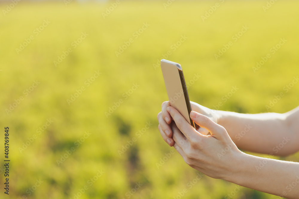 Close-up of smartphone in the hands of a girl against the background of a green field.
