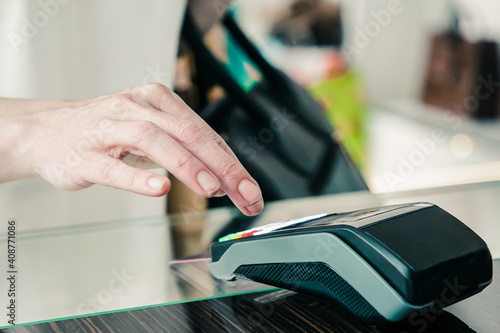 Customer paying for purchase by credit card in clothes store, entering pin code. Cropped shot, closeup of hands. Shopping or purchase concept © Mangostar