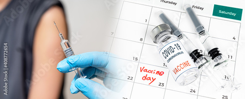 A doctor's hand holding a syringe and a calendar with the date of vaccination.