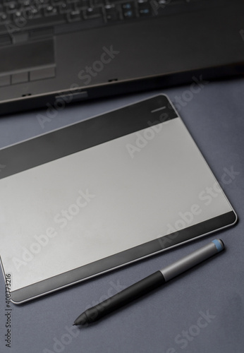 Graphic drawing tablet with pen on graphic designers desk, minimalist black and white background with blurred background