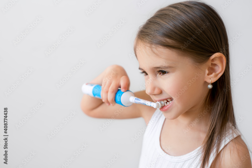 Child brushing teeth with electric toothbrush on white background. Dental hygiene. Copy space. Healthy baby teeth Child brushing teeth with electric toothbrush on white background. Dental hygiene. Copy space. Healthy baby teeth