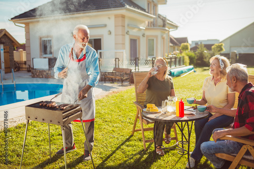 Elderly neighbors having backyard barbecue party by the pool