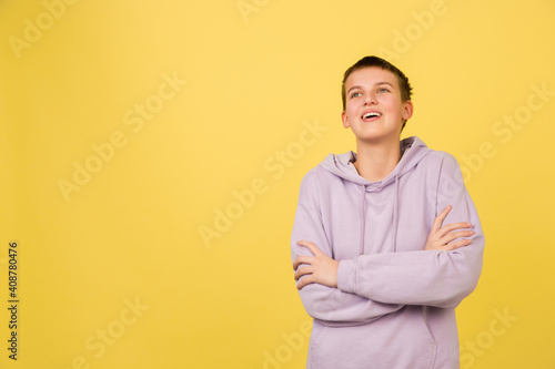 Looks inspired, hands crossed. Caucasian girl's portrait isolated on yellow background with copyspace. Beautiful female model in hoodie. Concept of human emotions, facial expression, sales, ad
