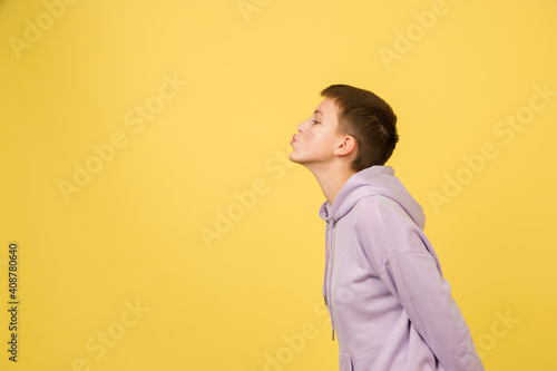 Kissing, sending kisses. Caucasian girl's portrait isolated on yellow background with copyspace. Beautiful female model in hoodie. Concept of human emotions, facial expression, sales, ad, fashion.