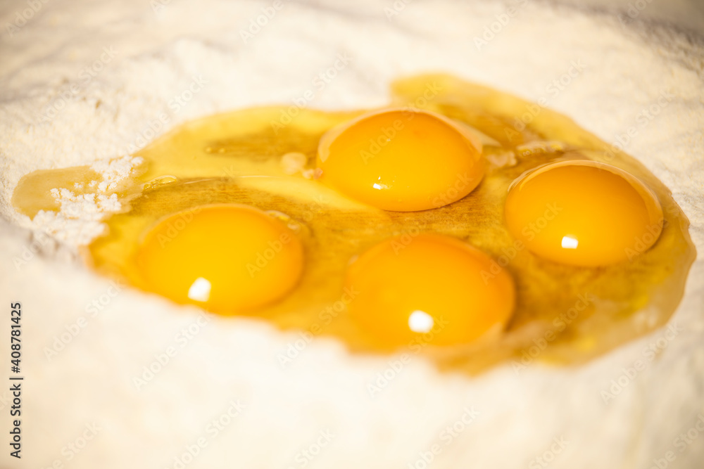 (Selective focus) Close-up view of a heap of flour with some fresh eggs inside. Flat lay, Ingredients for a homemade dough such as pasta, bakery, cakes etc. (Selective focus) Close-up view of a heap of flour with some fresh eggs inside. Flat lay, Ingredients for a homemade dough such as pasta, bakery, cakes etc.