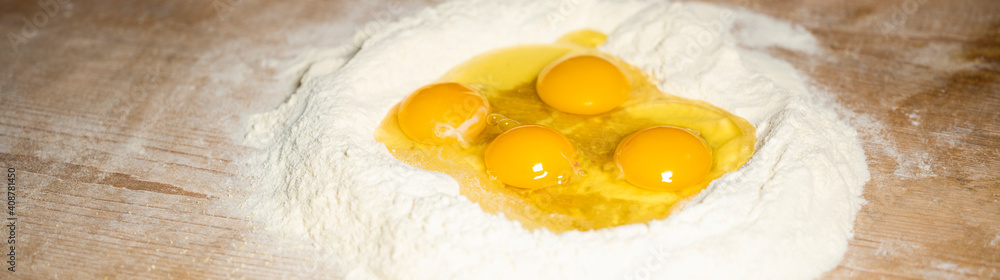 (Selective focus) Close-up view of a heap of flour with some fresh eggs inside. Flat lay, Ingredients for a homemade dough such as pasta, bakery, cakes etc. (Selective focus) Close-up view of a heap of flour with some fresh eggs inside. Flat lay, Ingredients for a homemade dough such as pasta, bakery, cakes etc.