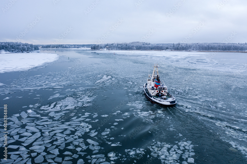 Fototapeta premium Tug boat pushing through the ice on a sea in winter
