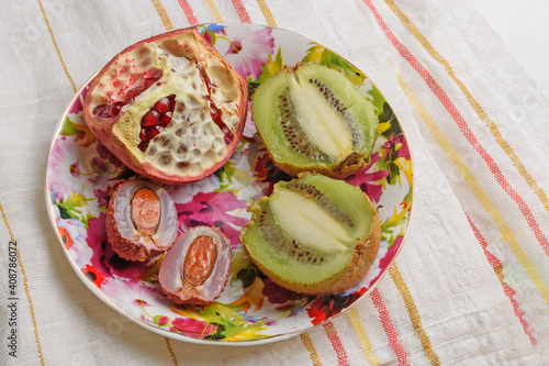 Pieces of kiwi, lychee and pomegranate on a colored plate on a fabric background