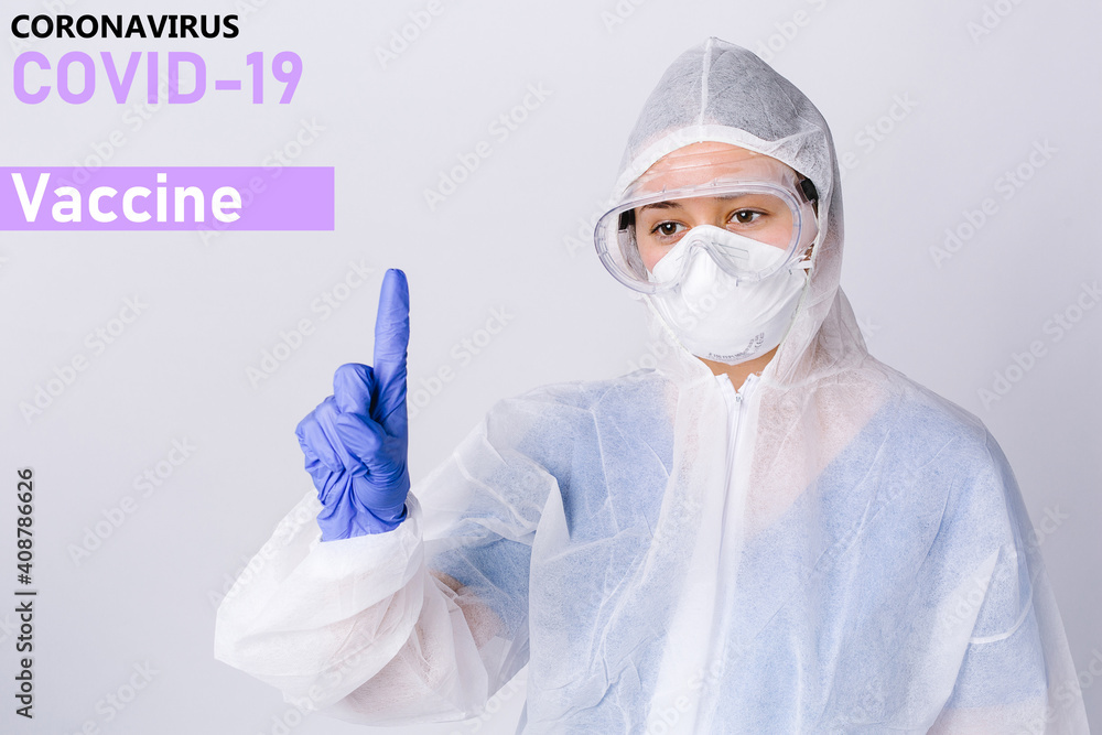 A doctor in protective glasses and coronavirus protect equipment points with his index finger to the top at the inscription about covid 19 vaccination. Fighting the virus on a gray background. A doctor in protective glasses and coronavirus protect equipment points with his index finger to the top at the inscription about covid 19 vaccination. Fighting the virus on a gray background.