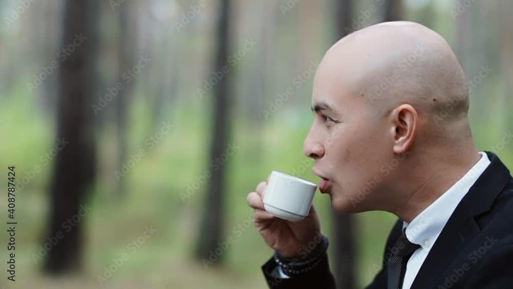 Bald man in a suit drinks coffee from a small cup Bald man in a suit drinks coffee from a small cup