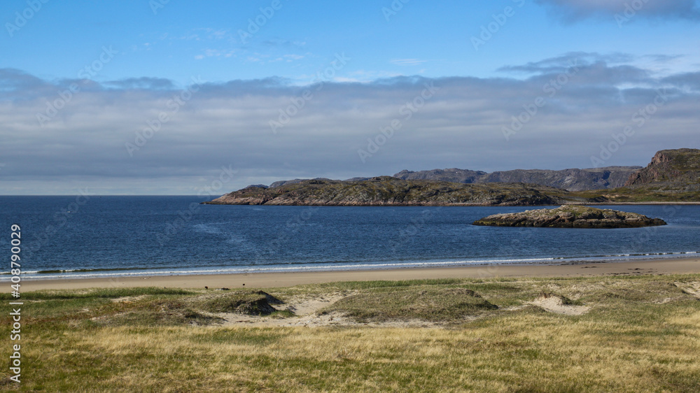 Beautiful sunny summer day in the north. Dark blue water of the  Barents sea bay.  A small island is lockated in the bay. Beauty of the northern Russia. Stone hills on the horizon.