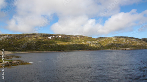 The sun's rays illuminate the hills on the opposite shore of the Barents Sea bay. View of the coast. Northern summer landscape. Snow in the hills in summer.