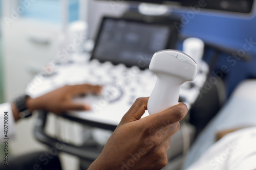 Close up photo of ultrasound scanner in the hands of male African American doctor. Diagnostics. Sonography. Modern ultrasound machine on the blurred background photo