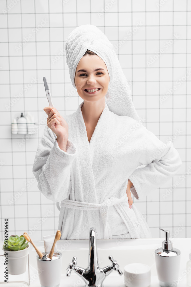 Smiling woman in towel showing pregnancy test in bathroom