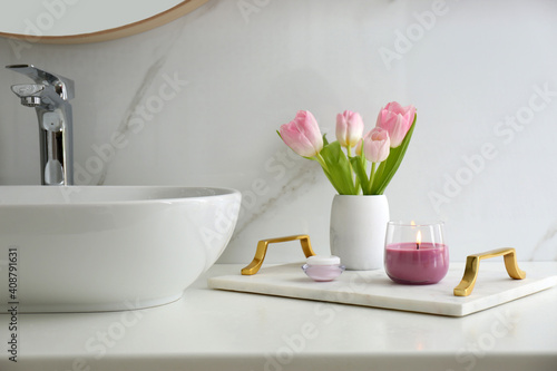 Beautiful flowers and candle on countertop in bathroom. Interior decor