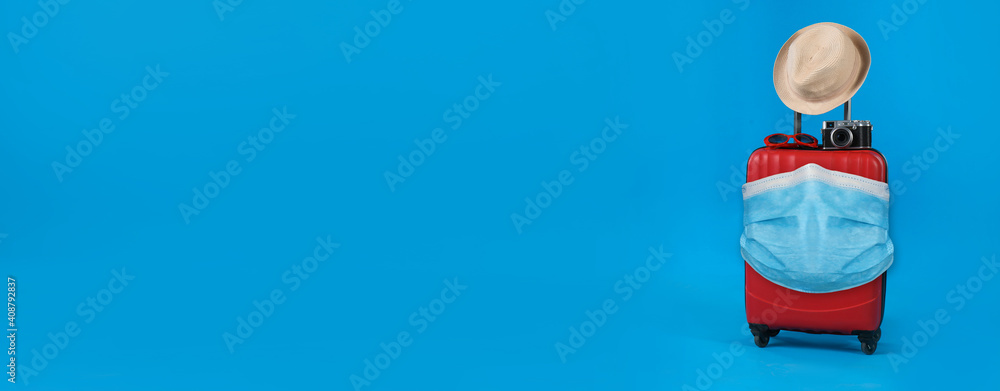 COVID-19 pandemic, travel during coronavirus outbreak. Suitcase with protective mask on blue background, space for text COVID-19 pandemic, travel during coronavirus outbreak. Suitcase with protective mask on blue background, space for text