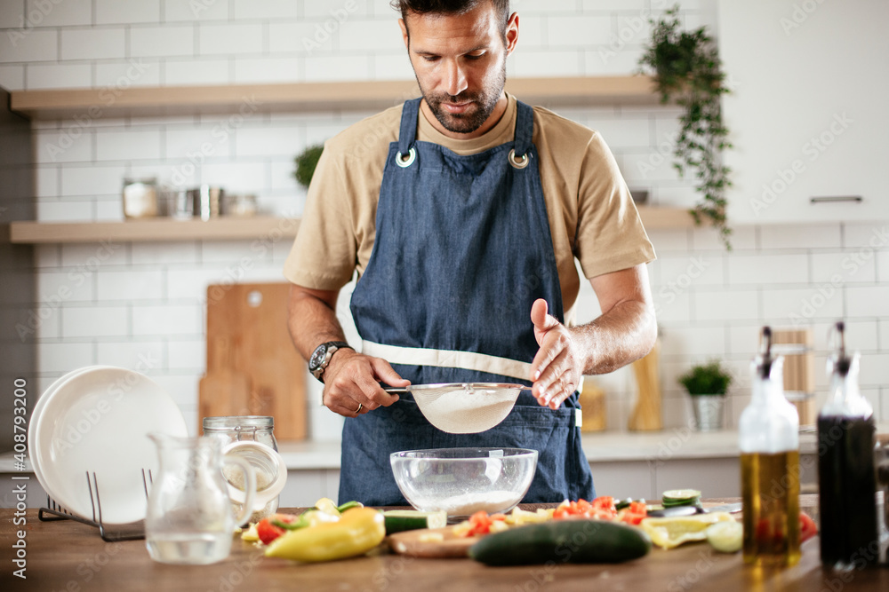 Attractive man cooking in modern kitchen. Handsome man playing with flour while preparing delicious food. Attractive man cooking in modern kitchen. Handsome man playing with flour while preparing delicious food.