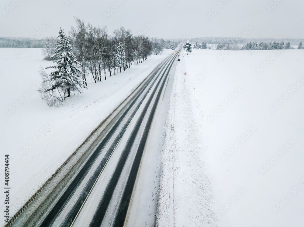 Obraz premium Drone view of a paved road with cars with their headlights on in the distance on a winter cloudy day. Beautiful winter landscape