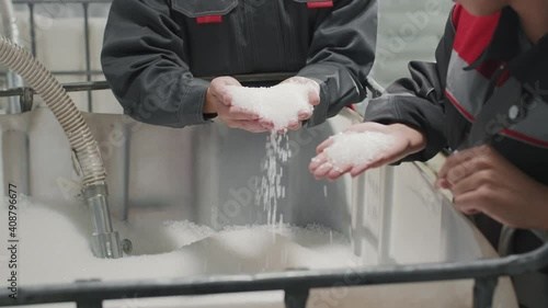 Midsection slow-motion footage of unrecognizable factory workers standing by big container with polypropylene granules holding them in hands and pouring