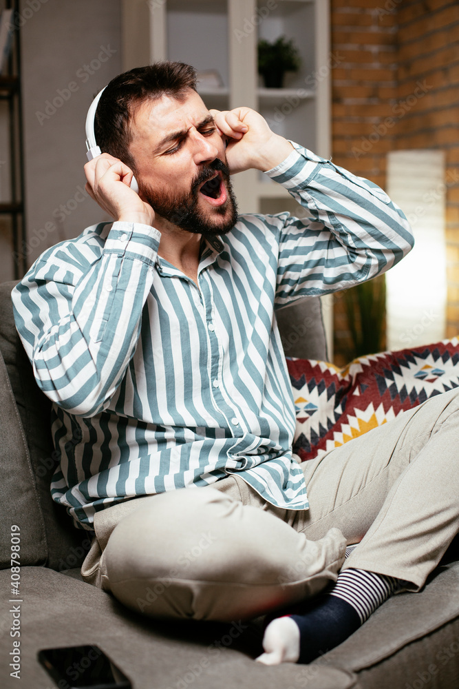 Young man with headphones resting on sofa. Happy man singing and listening the music.