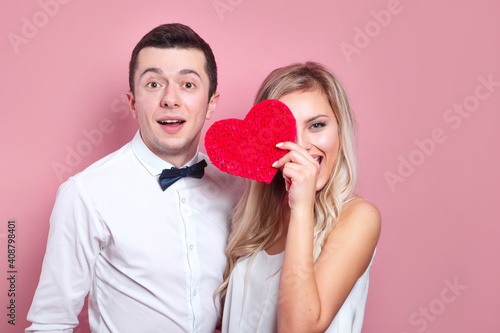 Valentines day. Surprised happy couple holding paper heart on pink background