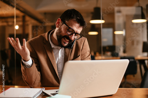 Handsome man talking to the phone at his workplace. Young businessman using laptop in his office