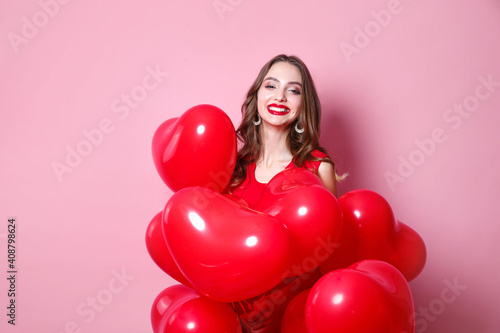 Woman on Valentines Day. Beautiful elegant young woman with heart shape red air balloons on pink background. © Elena Kratovich