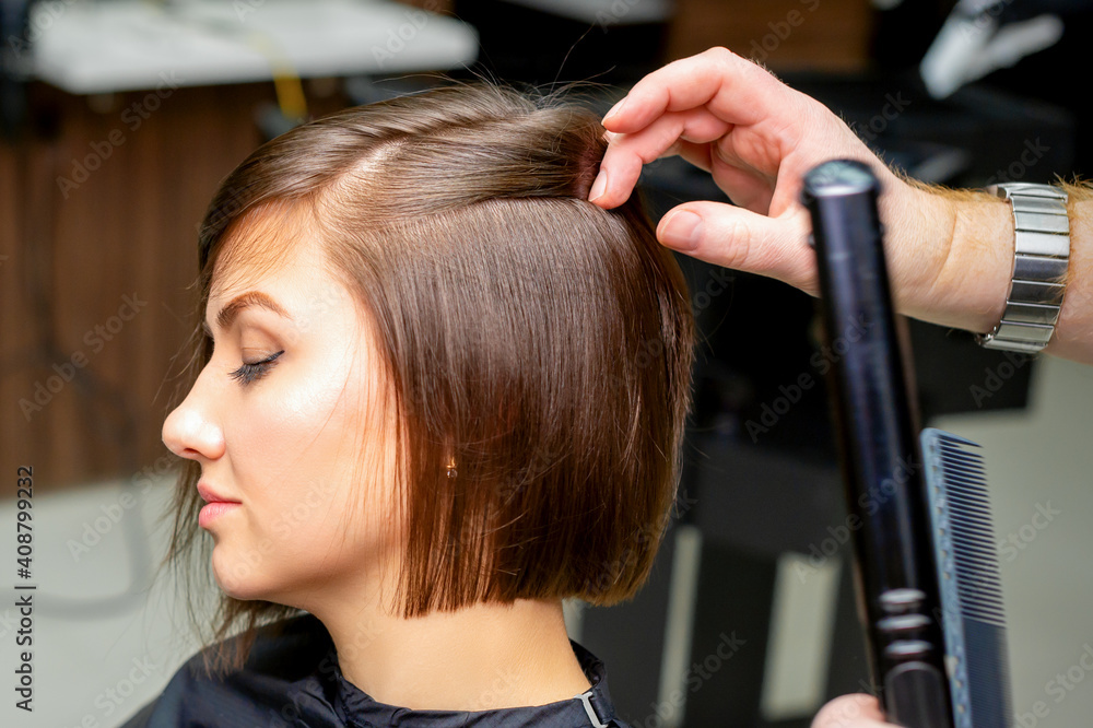 Fototapeta premium A male hairdresser is straightening the hair of the young woman in a beauty salon