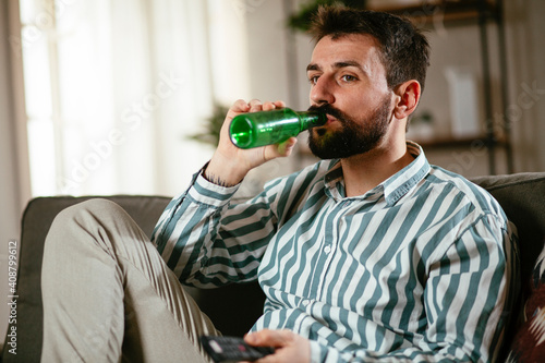 Young man at home. Man sitting in living room watching movie and drinking beer..